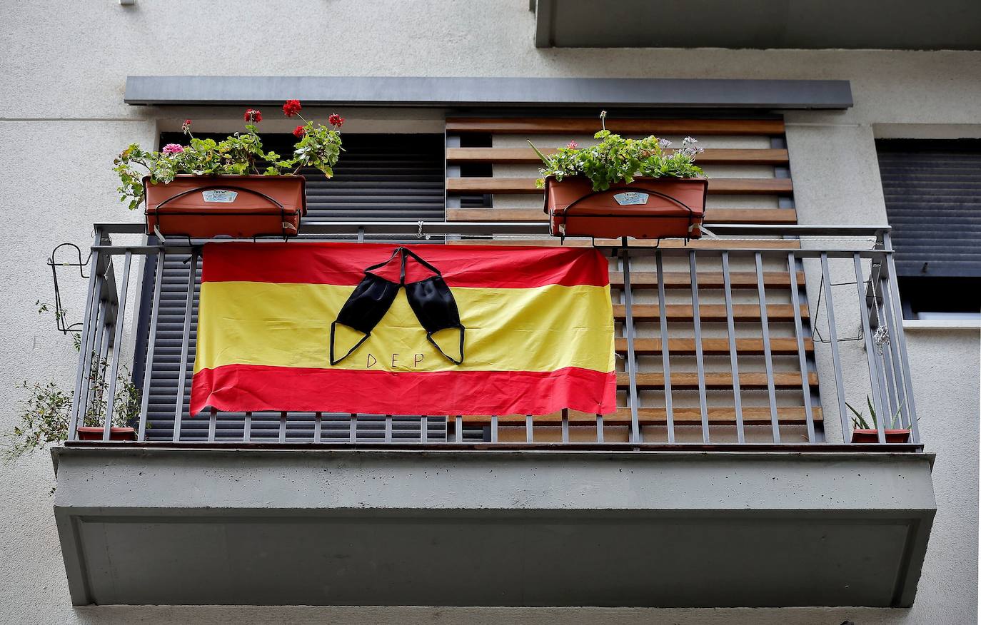 Una bandera de España cuelga de un balcón con dos mascarillas negras a modo de crespón por las víctimas del coronavirus