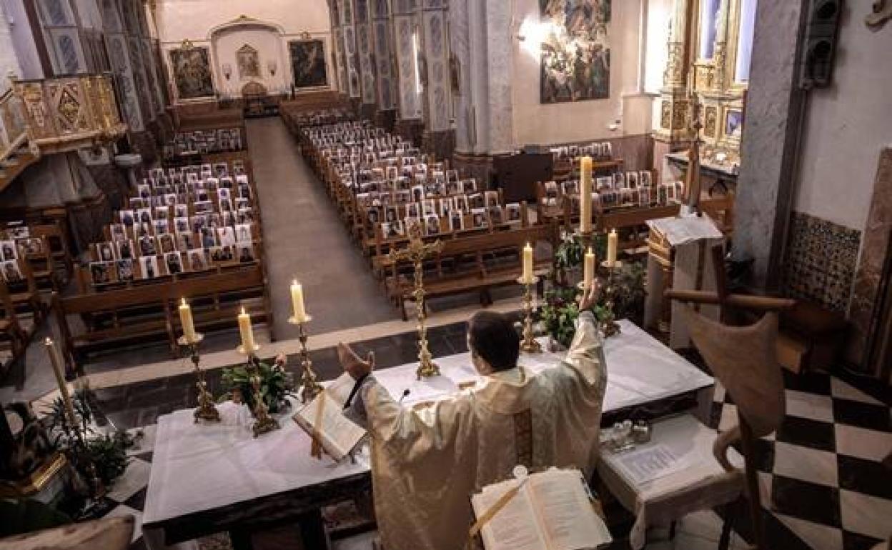 Un sacerdote celebra las misas a puerta cerrada acompañado por las fotografías de sus feligreses.