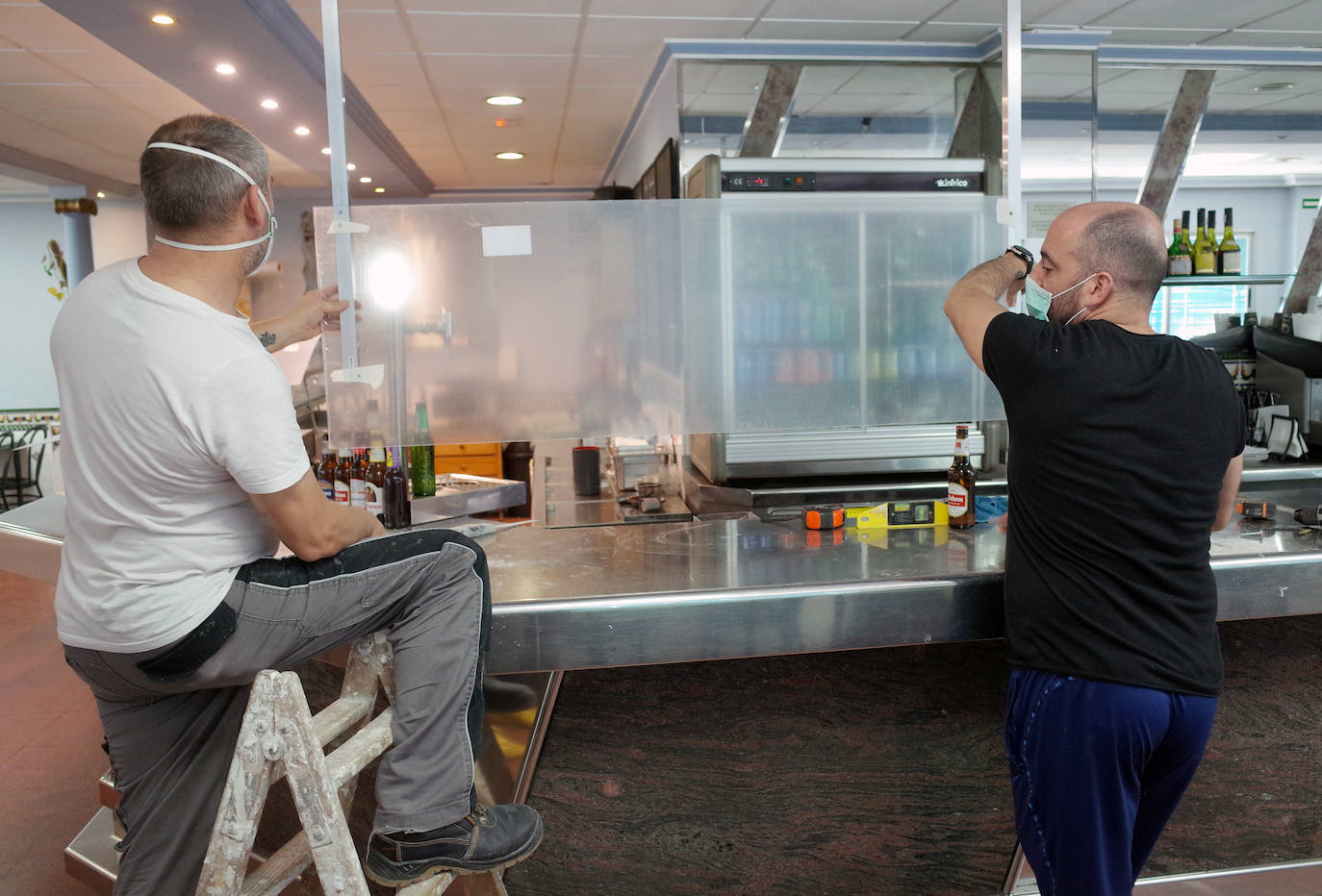 Dos operarios colocan mamparas de metacrilato en la barra de un restaurante del polígono Vara de Quart, en Valencia