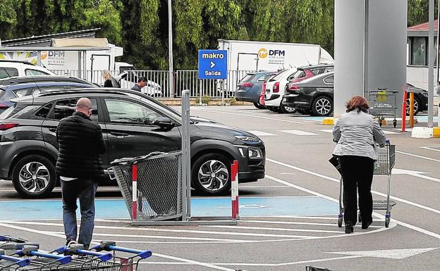 Imagen principal - Dos clientes de Makro, ayer, en el aparcamiento de la empresa mayorista | Jorge Dasí saca de su coche los productos alimenticios que compró ayer para su pizzería de El Saler.