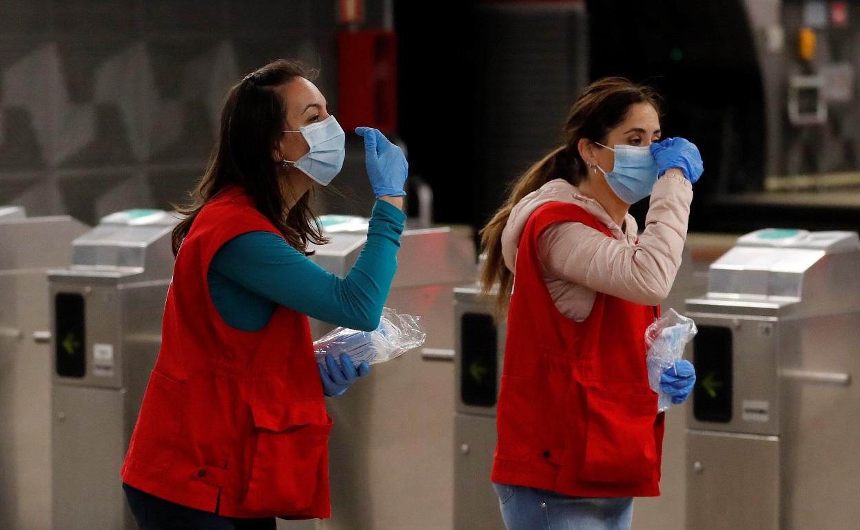 Dos miembros de Cruz Roja reparten mascarillas quirúrgicas. 