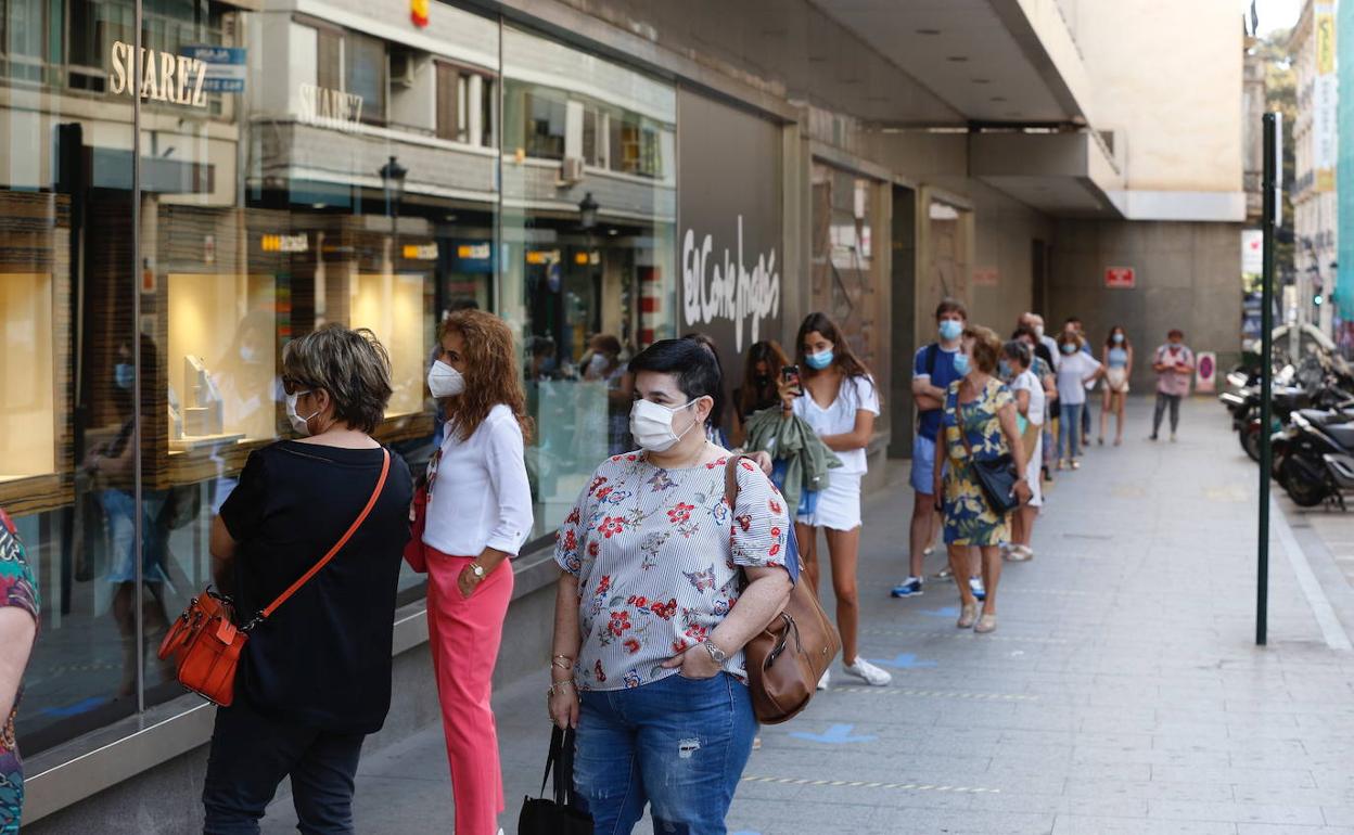 Varios personas esperan la entrada en las puertas de El Corte Inglés. 