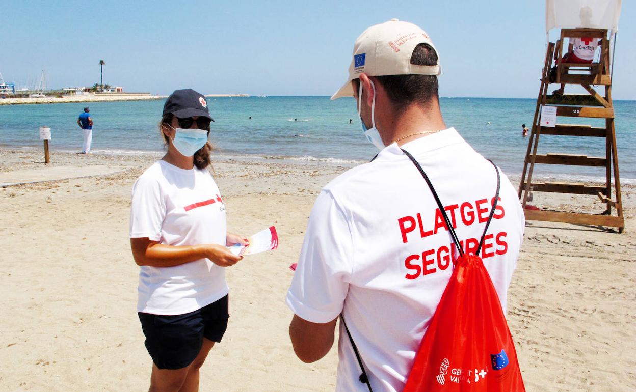 Un auxiliar de playa conversa con una miembro de Cruz Roja en el litoral de Dénia.