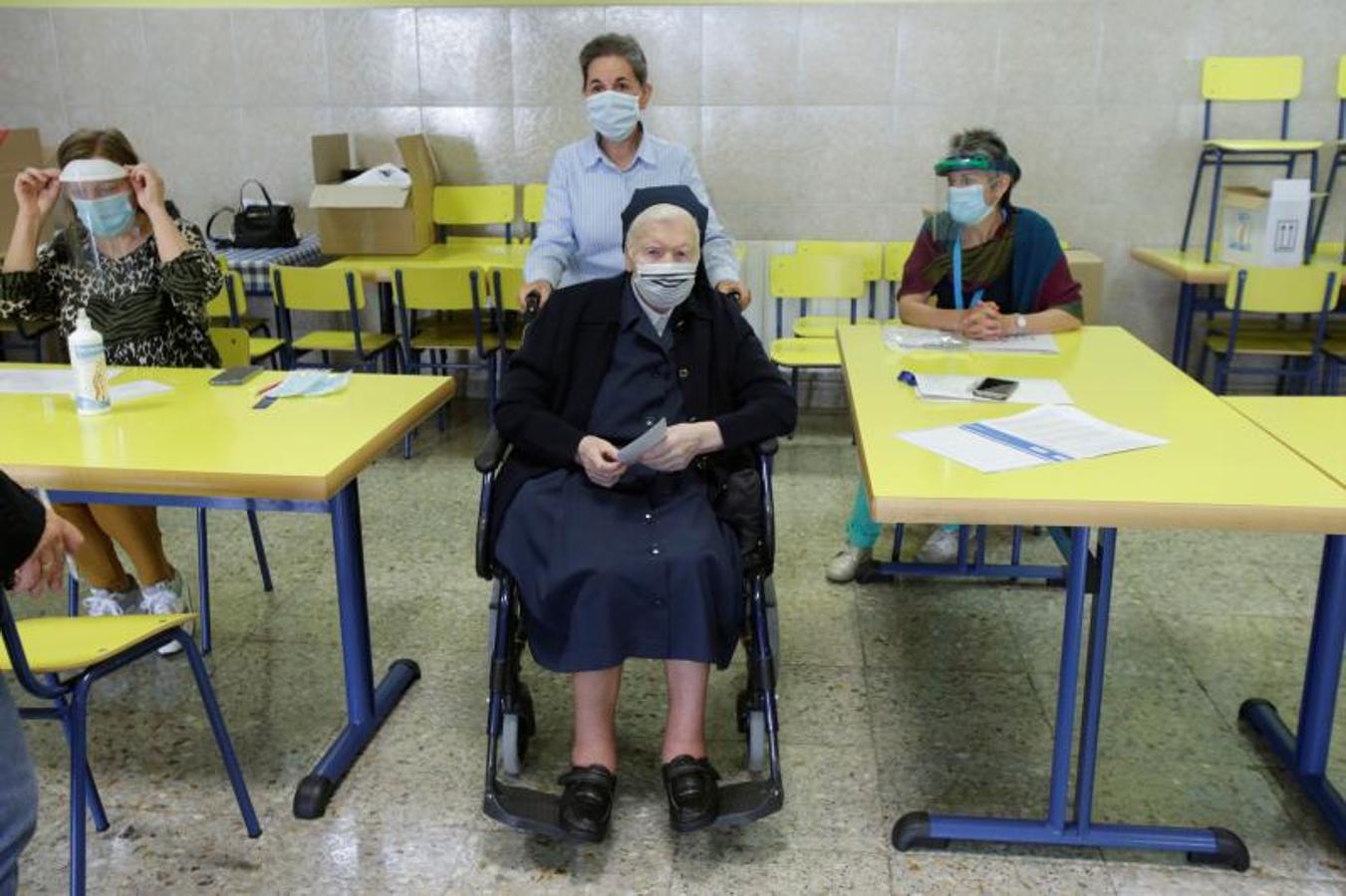 Una monja, con mascarilla, es acompañada antes de emitir su voto en un colegio electoral en Ribadeo
