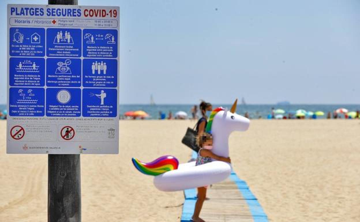 Una niña y una mujer en la playa, ambas con mascarillas.