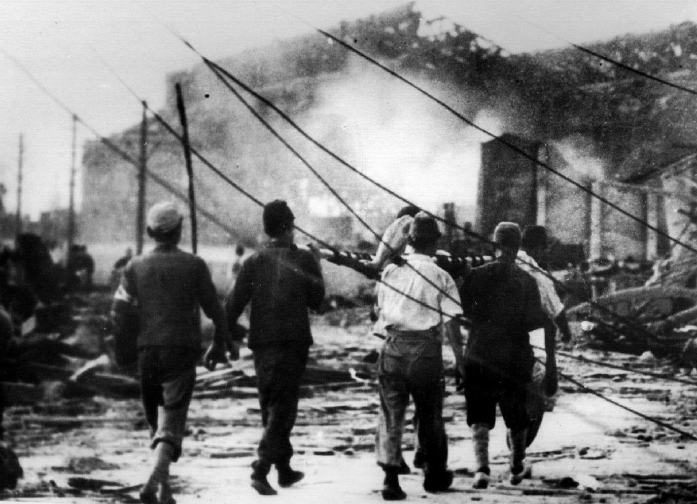 Trabajadores aéreos japoneses llevan a una víctima de la bomba atómica lejos de las ruinas humeantes en Hiroshima.