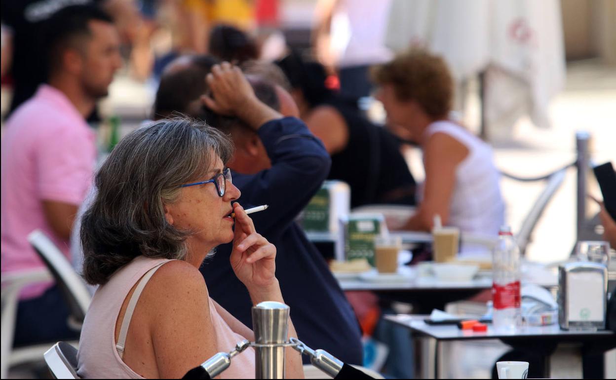 Una mujer fuma sentada en una terraza. 