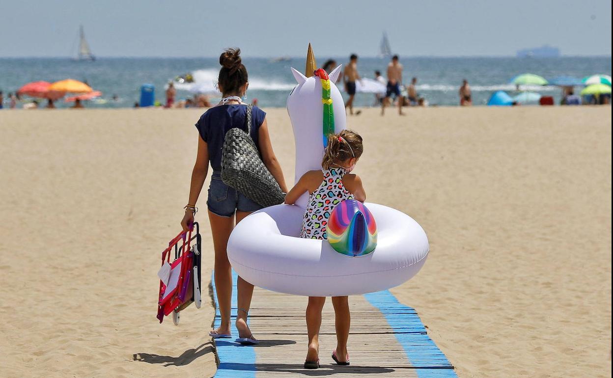 Una niña carga con su flotador hacia la orilla de la playa de las Arenas.