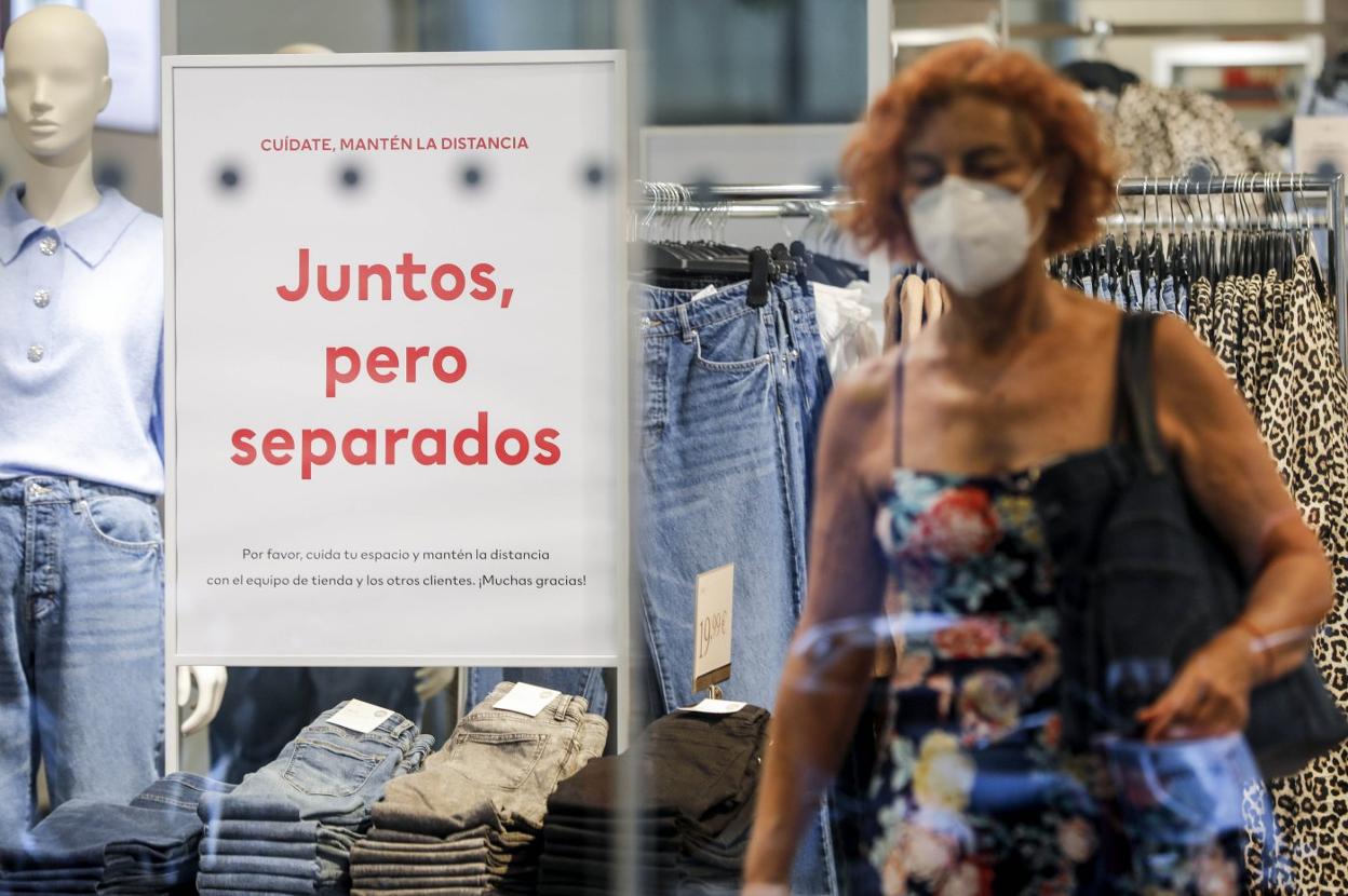 Una mujer con mascarilla en un comercio donde informan de las medidas de seguridad obligatorias en el interior del local. irene marsilla