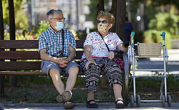 Dos personas mayores se protegen del sol con la sombra de un árbol. 