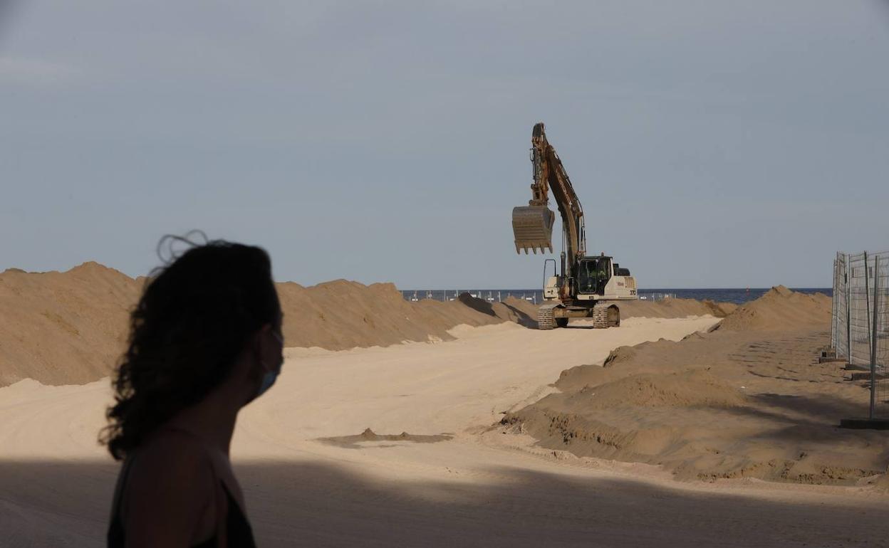 Una viandante observa, ayer, el trasvase de arena en la playa del Cabanyal. 