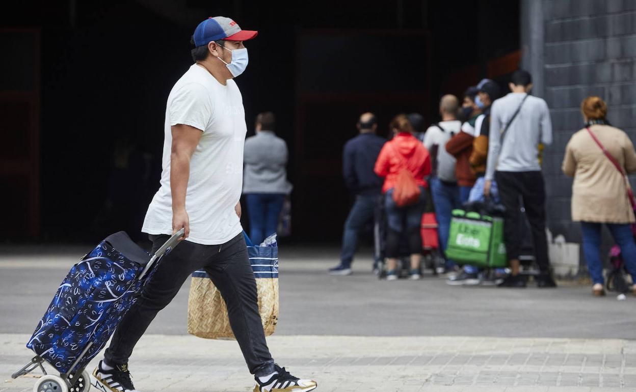 Un hombre arrastra el carro de la compra mientras varias personas aguardan su turno en la cola del reparto de alimentos. 