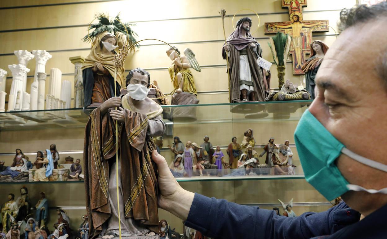 Un comerciante con mascarilla coloca figuras de un belén en el estante. 