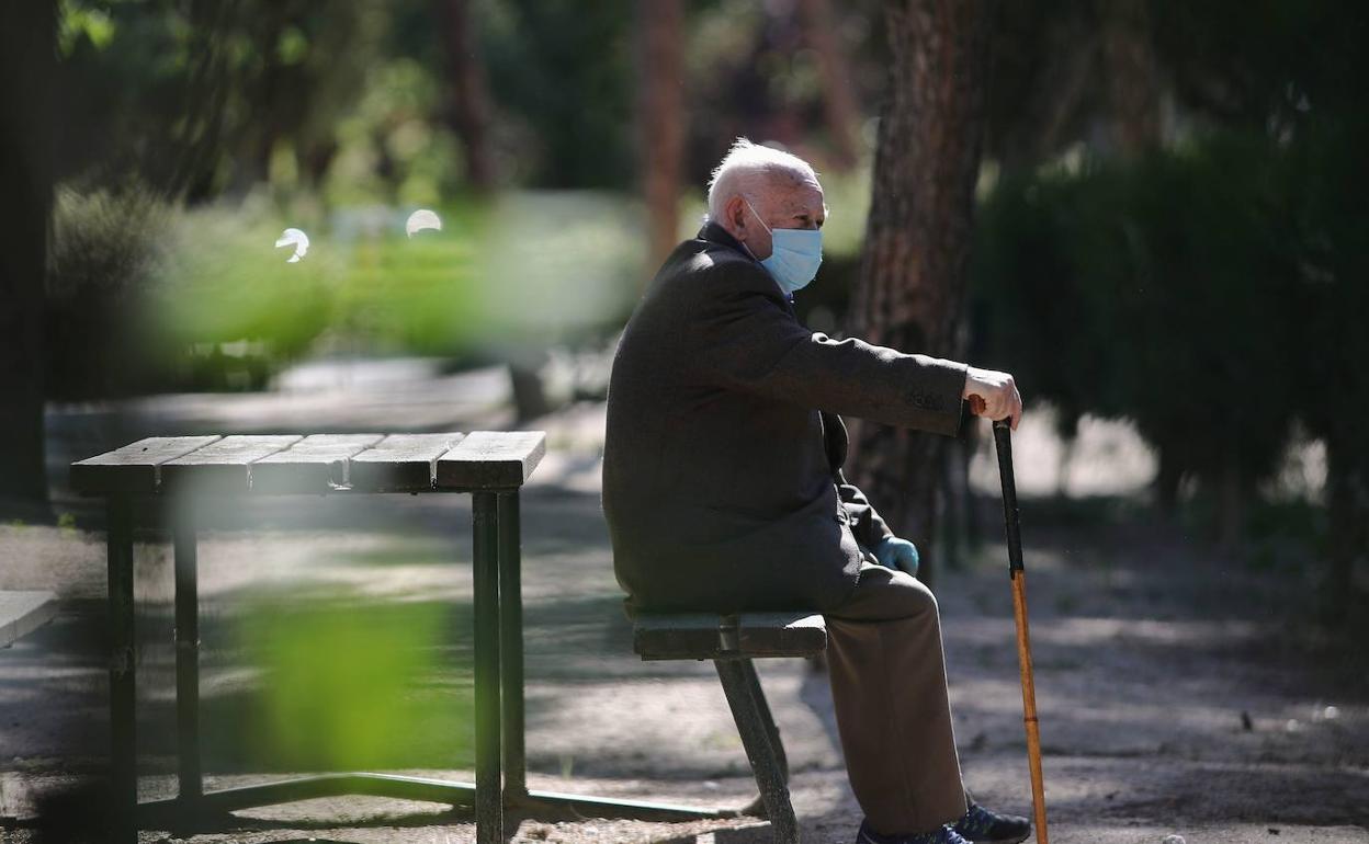 Un hombre sentado en un banco con mascarilla. 