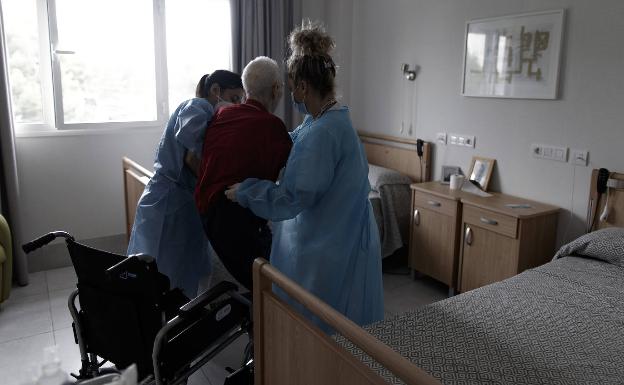 Trabajadoras de un centro de mayores ayudan a un anciano a sentarse en una silla de ruedas