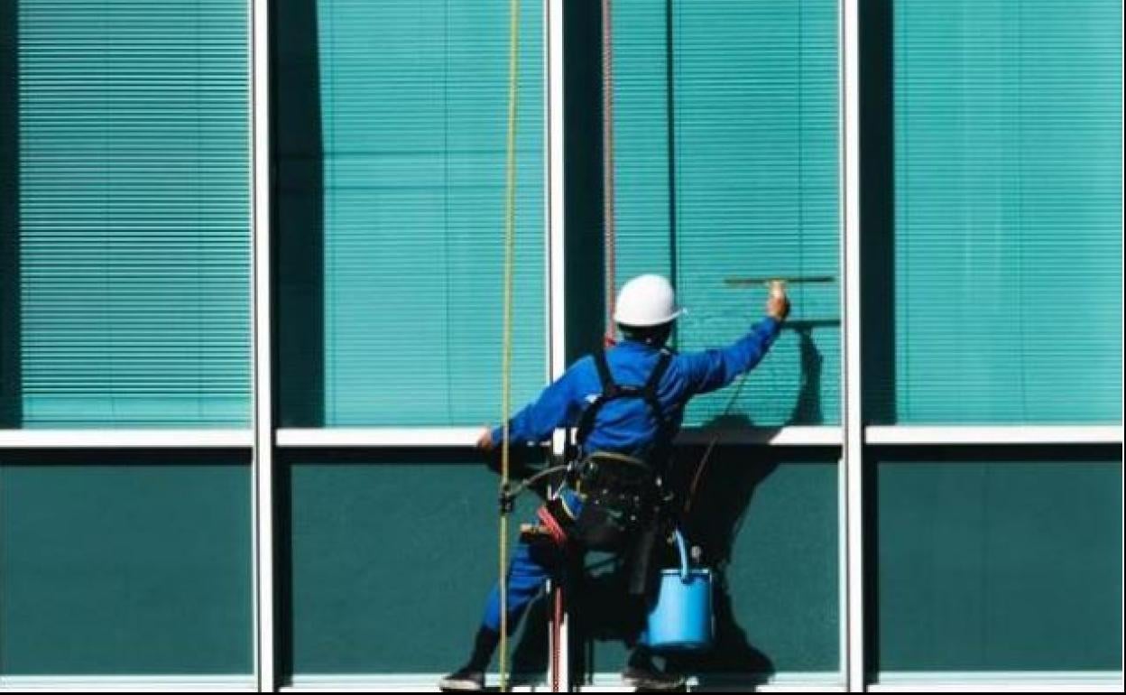 Un trabajador limpia cristales en un edificio. 