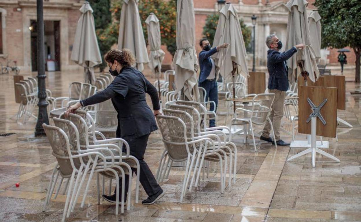 Unos trabajadores de un restaurante del centro de Valencia recogen la terraza cumpliendo con las nuevas medidas para la hostelería y el cierre anticipado a las 17h. de la tarde