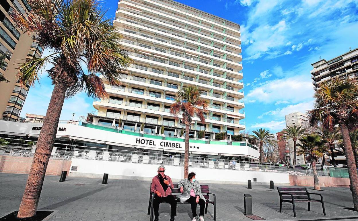 Dos personas sentadas ante un establecimiento hotelero de Benidorm. 