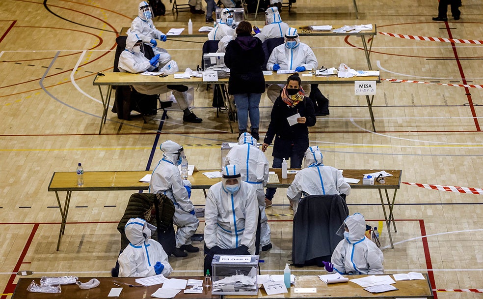 Varias personas vestidas con equipos de protección individual (EPI), trabajan en las mesas electorales del Polideportivo Municipal de la España Industrial de Barcelona.