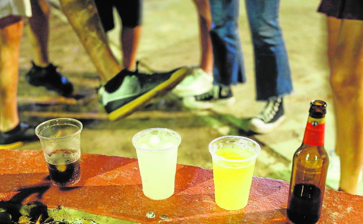 Vasos de plástico con refrescos y alcohol apoyados sobre el murete del jardín en la plaza de Honduras, junto a unos jóvenes.