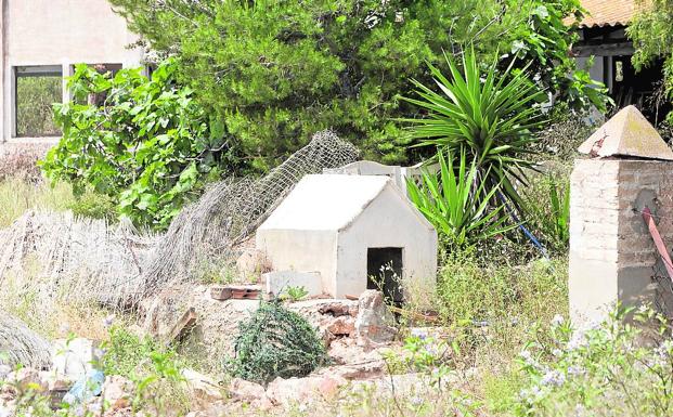 Imagen principal - Caseta del perro. 'Erty' era el nombre de la perra con la que convivía la pareja y sus hijos en la parcela. (Damián Torres) | Ruina. En esta deteriorada nave próxima a la casa también jugaban los niños. Todavía hay dentro juguetes que penden de una cuerda. (Damián Torres) | Vecinos y amigos de la familia honran el recuerdo de los menores con juguetes, flores y rosarios en su nicho.