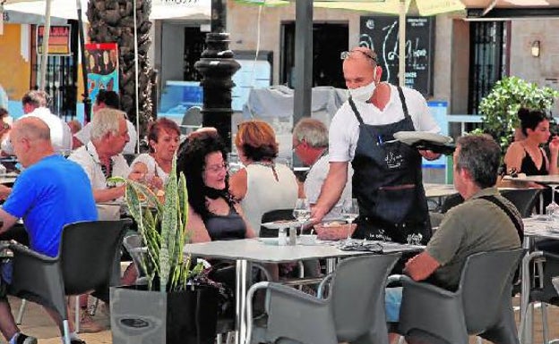 Un camarero sirve la comida a unos clientes en la terraza de un restaurante de Dénia.