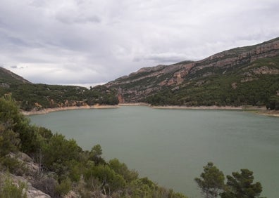 Imagen secundaria 1 - Arriba, vista aérea del pantano de Bueso. Abajo a la izquierda, el pantano desde la orilla. A la derecha, bañistas observan el islote del pantano. 