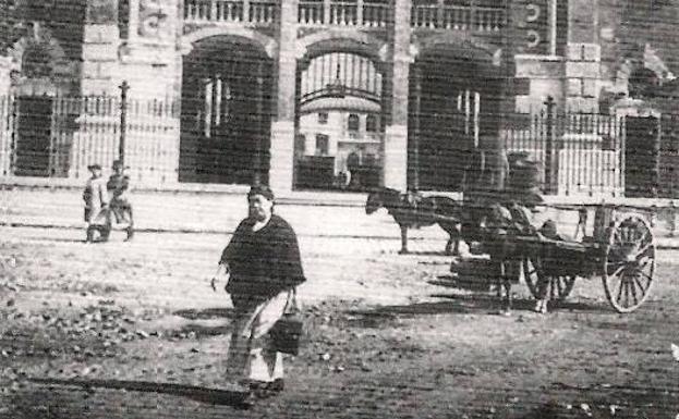 Ciudadanos caminan por la puerta del mercado, en una imagen de principios de siglo XX, cuando aún se empleaban carros de tracción animal.