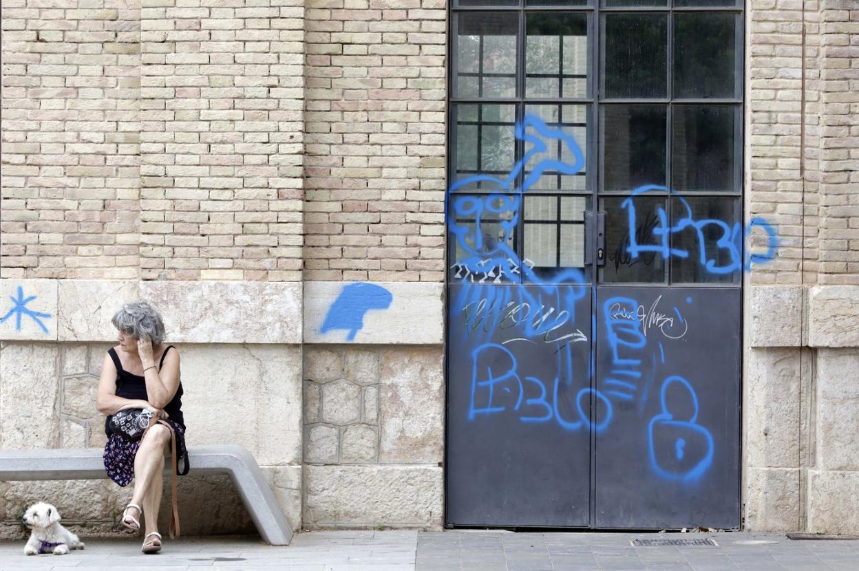 Una vecina descansa en un banco junto a una de las naves del Parque Central repleta de pintadas, ayer. irene marsilla