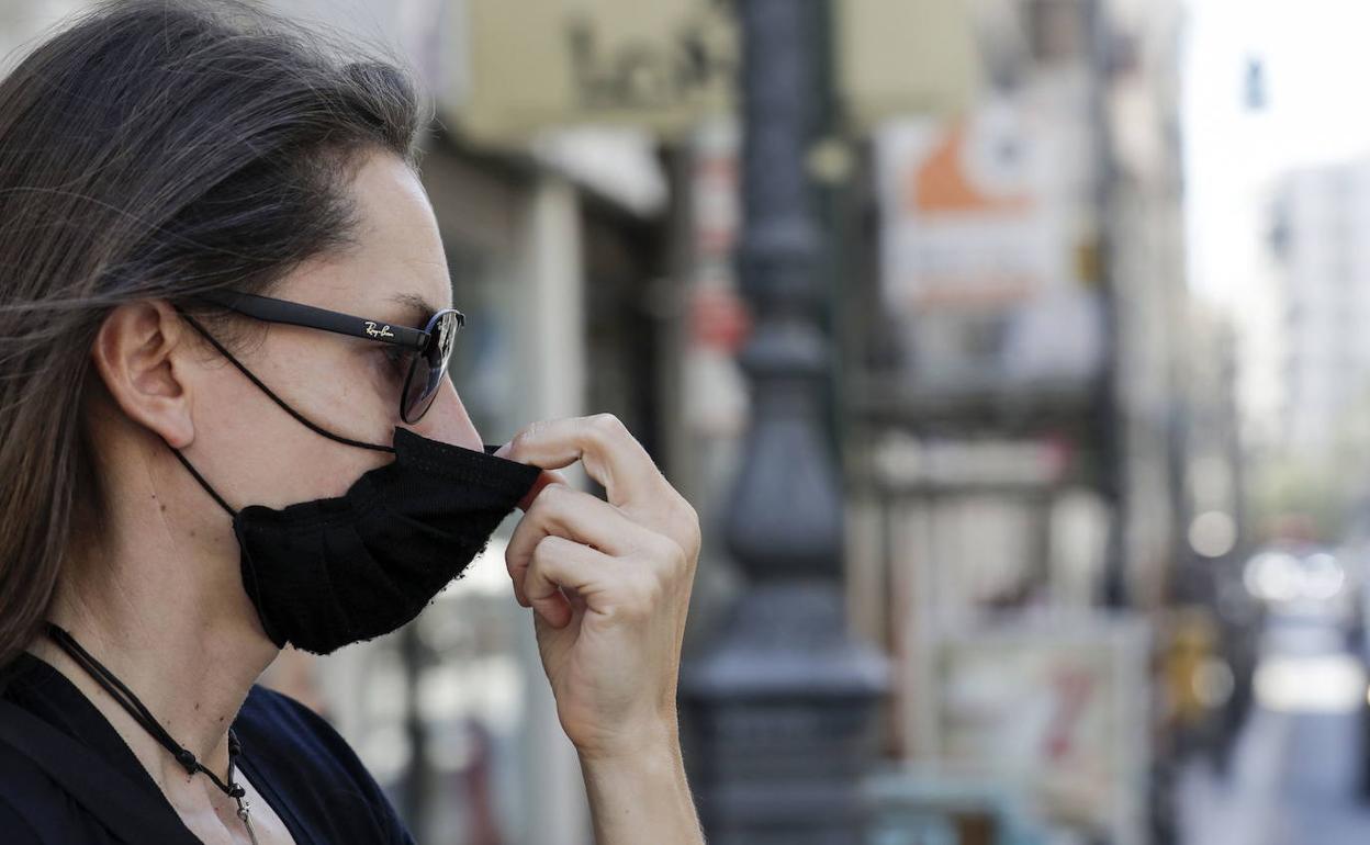 Una mujer se coloca la mascarilla en una calle de Valencia.