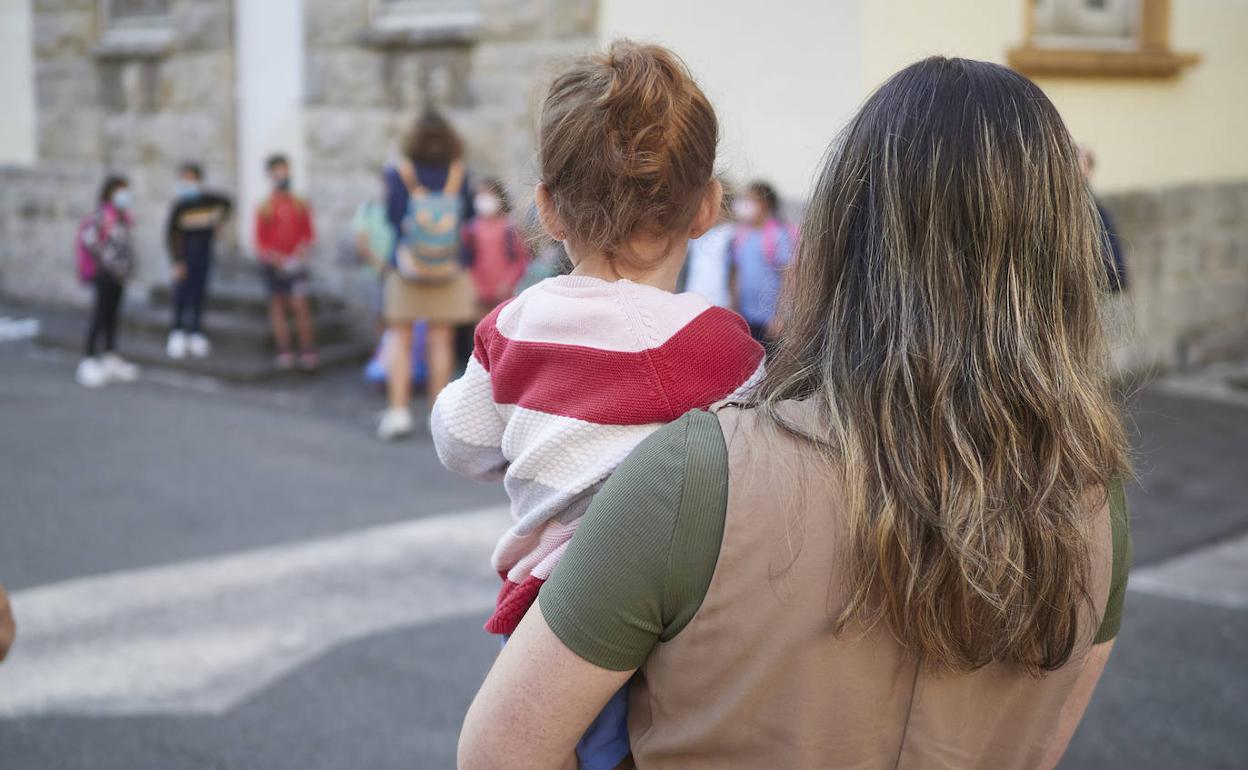 Una madre con su hija en brazos el primer día de colegio. 