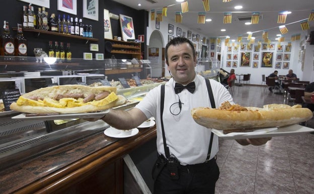 Raúl Bermejo sirve dos bocadillos XXL, que han atraído a muchos comensales. Las banderitas con la señera cuelgan en el techo.