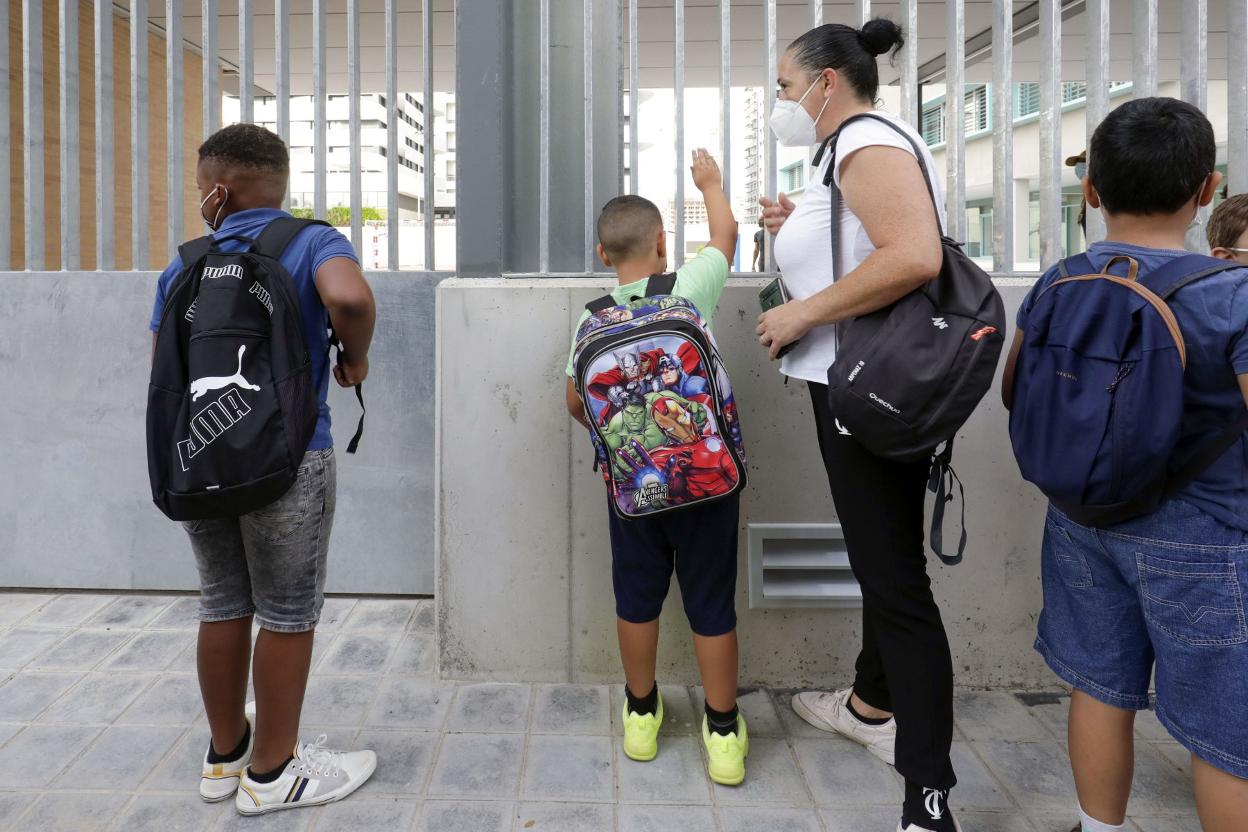 Uno niño saluda a otro desde el exterior del centro educativo. irene marsilla