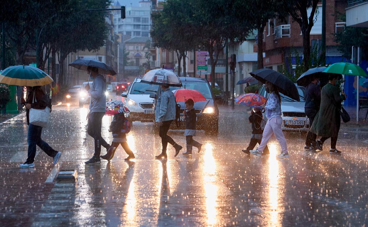 Varias personas cruzan por una calle de Gandia durante las lluvias de esta mañana. 