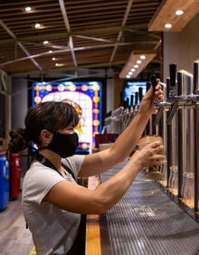 Imagen secundaria 2 - Arriba, estanterías de la cervecería Cervezas del Mercado de Colón. Abajo a la izquierda, la terraza del bar El León, con la Plaza Redonda al fondo. Abajo a la derecha, una mujer tira una cerveza en uno de los dieciocho grifos de Cervezas del Mercado de Colón.