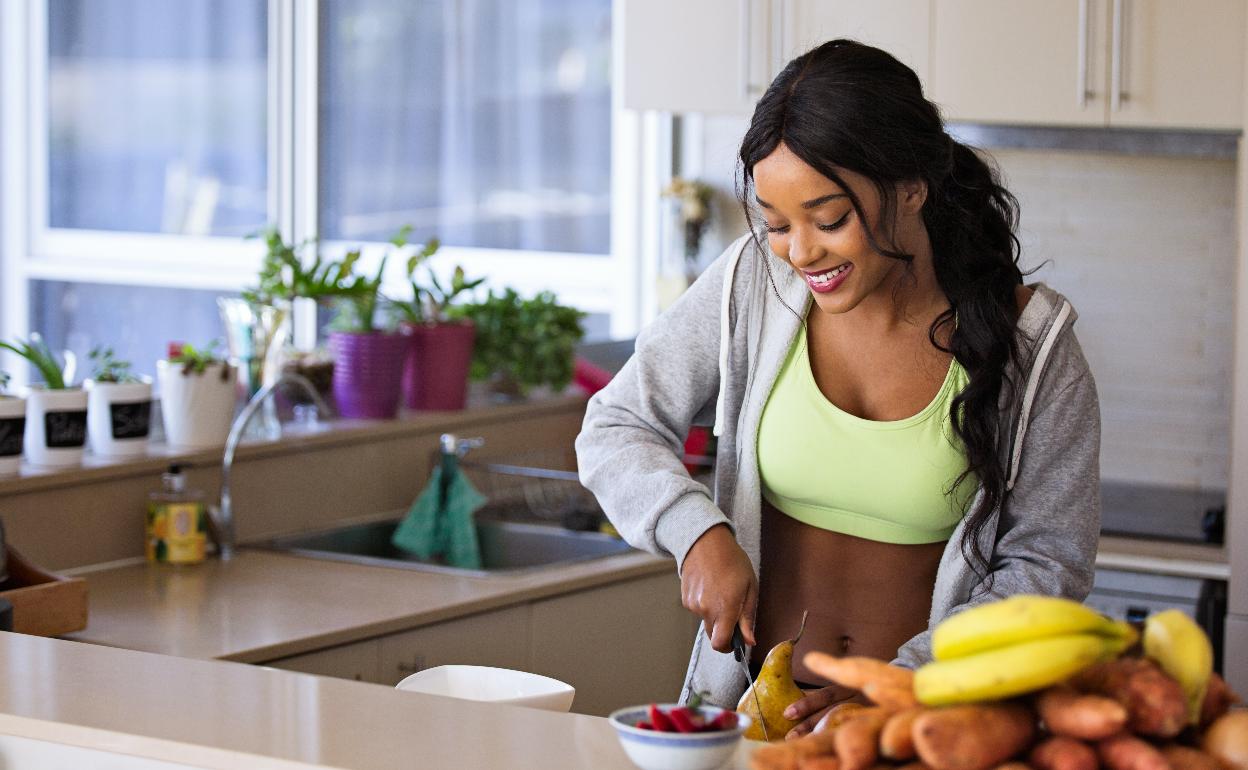 Una deportista corta fruta en la encimera de una cocina. 