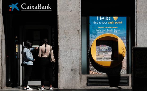 Dos jóvenes utilizan un cajero de Caixabank. 