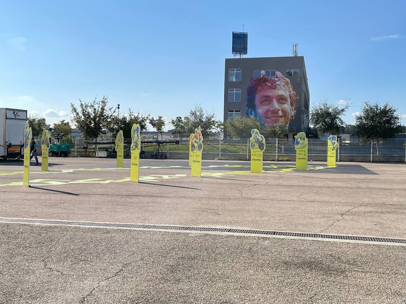 El paddock se ha teñido de amarillo este fin de semana. Como las gradas, que el sábado ya han expresado una muestra de intención de lo que será la carrera de este domingo. No es para nada exagerado afirmar que el 70% de los aficionados lucían merchandising de Valentino Rossi. Entre las muestras de homenaje que se le han dedicado por el momento, destaca la exposición de las nueve motos con las que ha sido campeón del mundo. Al lado está la 'Piazza Valentino Rossi', rotulada con una placa que simula ser de mármol y donde hay unos paneles amarilos que expresan los principales hitos del mito transalpino a lo largo de su carera. Más allá de esto, la mayoría de los camiones de los equipos tienen un panel, del mismo diseño, como muestra de gratitud al piloto por haber potenciado el Mundial de MotoGP durante sus más de 25 años de carrera. El propio piloto, en su mono, luce en la parte posterior este fin de semana un escueto pero representativo: 'Grazie'.