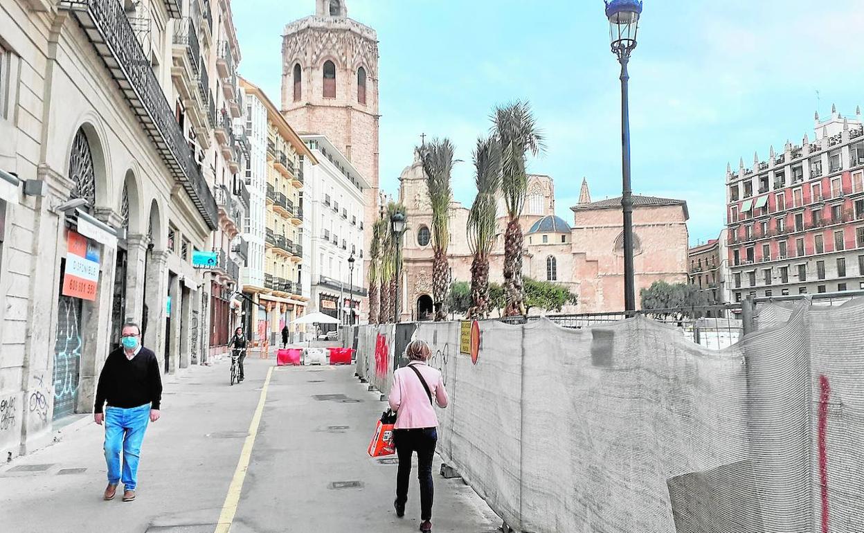 Unos viandantes pasan junto a la zona de obras de la plaza de la Reina. 