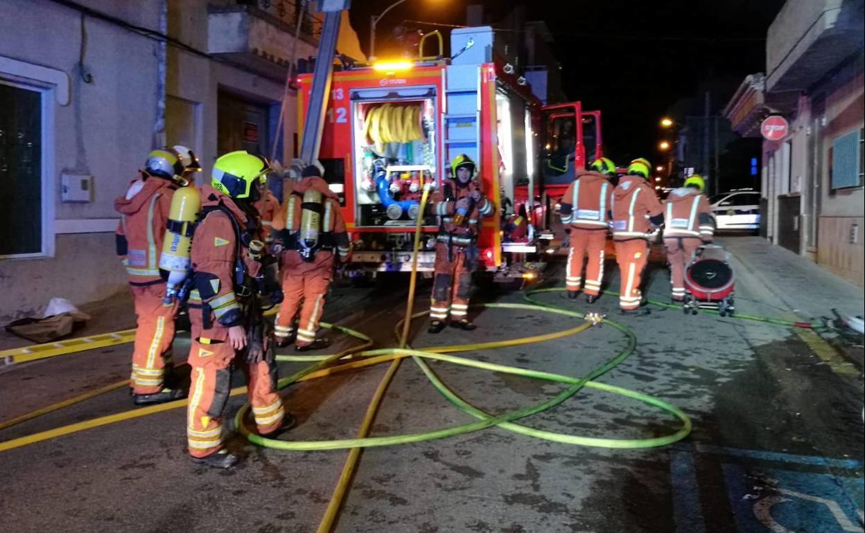 Un grupo de bomberos desplegados junto a la vivienda incendiada, en la calle Primero de Mayo de Ribarroja. 