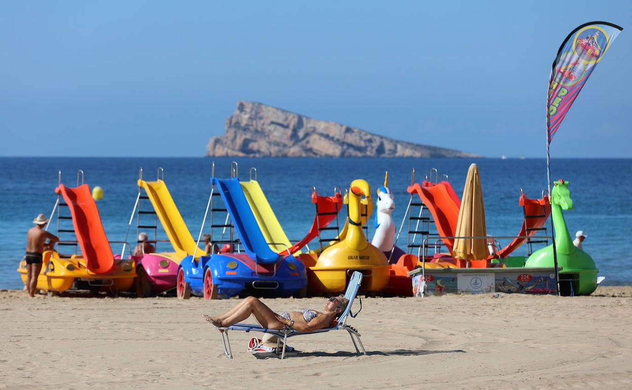 Pantines de agua y una persona tomando el sol en una playa de Benidorm. 