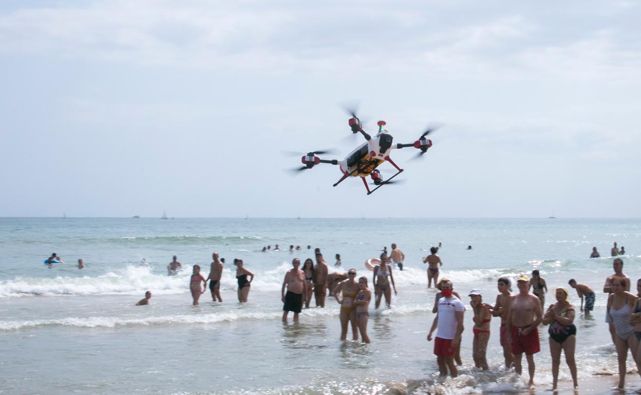 Un dron vuela sobre la playa de Gandia ante la mirada de los bañistas. 