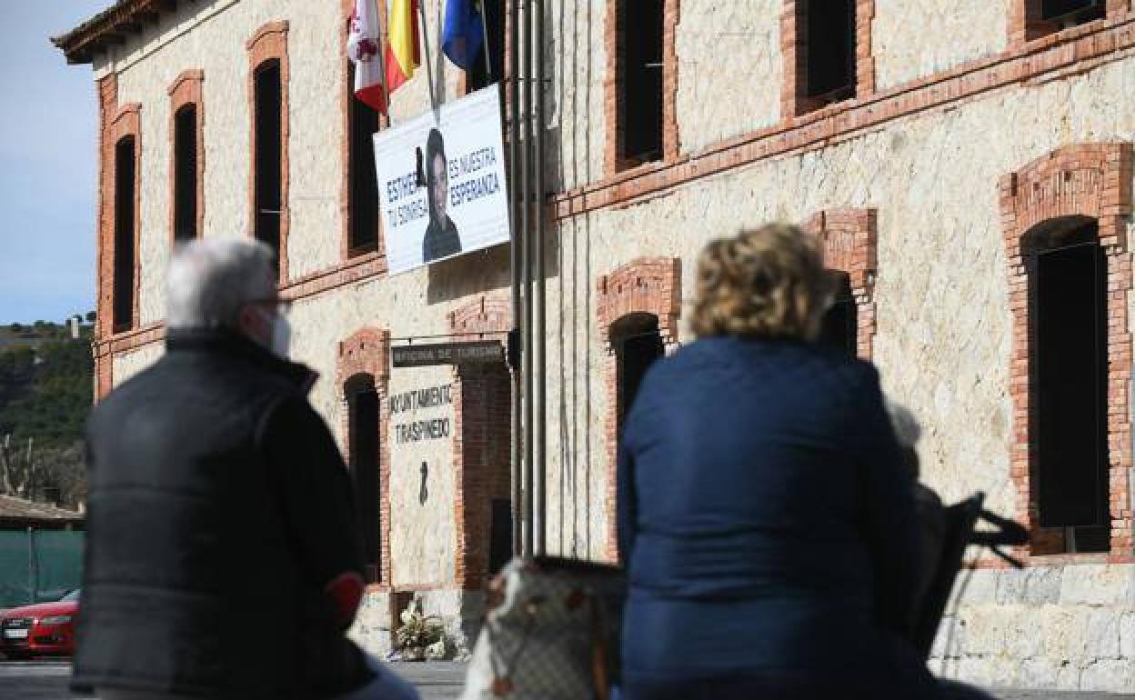 Dos vecinos de Traspinedo (Valladolid), sentados en los bancos de la plaza del Ayuntamiento. De fondo, el cartel que rememora a Esther López. 