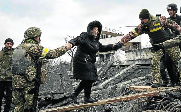 Los soldados ayudan a una mujer a cruzar sobre los escombros de un puente destruido a unos kilómetros de Kiev. 