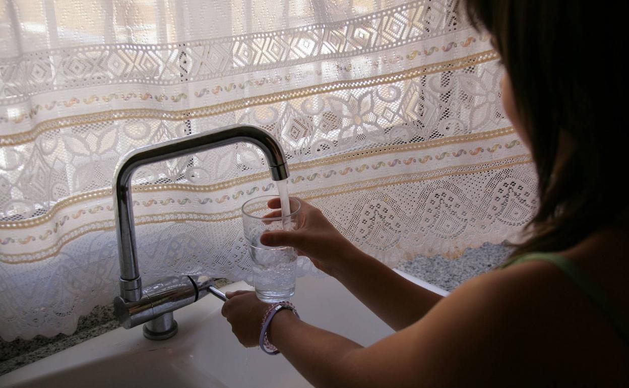 Una mujer llena un vaso de agua en su casa. 