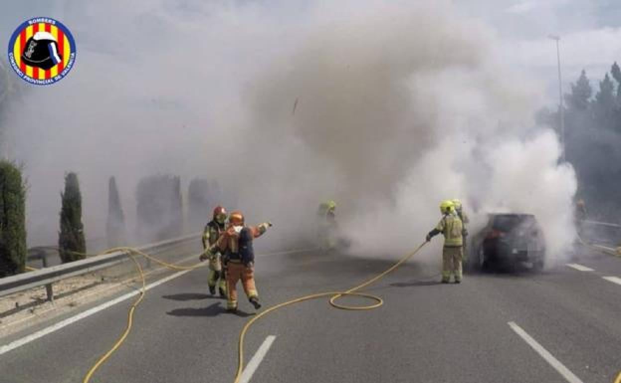 Los bomberos apagan el fuego del coche calcinado. 