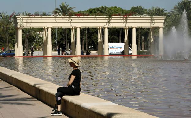 Una mujer disfruta del buen tiempo sentada junto a una de las fuentes en los Jardines del Turia. 