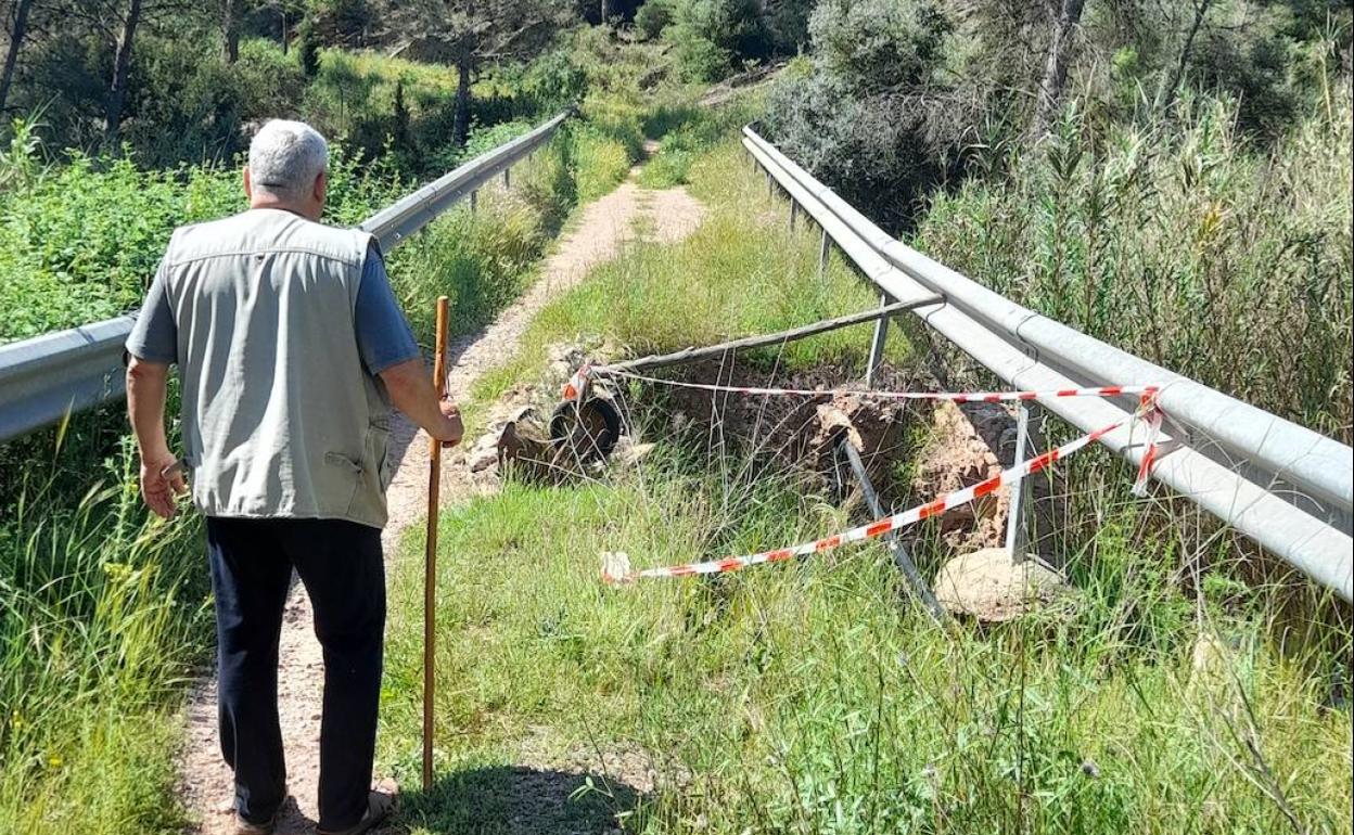 Un hombre circula por el puente y, frente a él, el agujero sin reparar, con una carretilla y un fino tronco. 