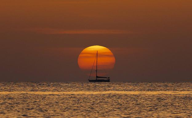 Un barco navega al amanecer frente a la playa de Las Rotas de Denia. 