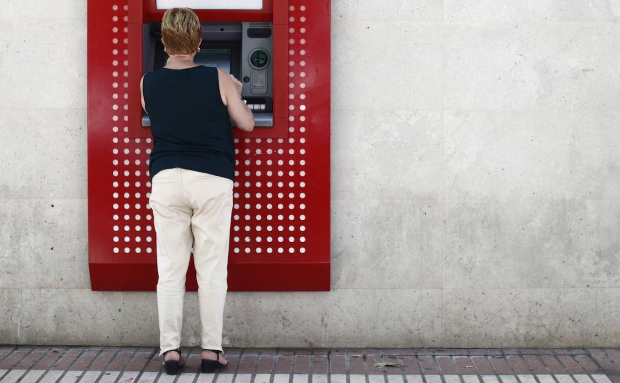 Una mujer sacando dinero de un cajero. 